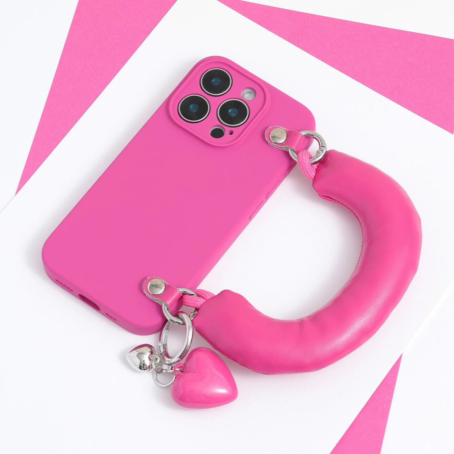 Bright fuchsia phone case with an oversized padded handle and two heart charms, displayed on a pink and white background.
