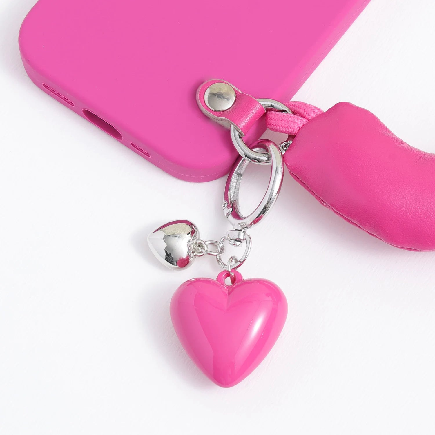 Close-up of a pink heart charm and silver heart charm attached to a fuchsia handle phone case with silver-tone hardware.