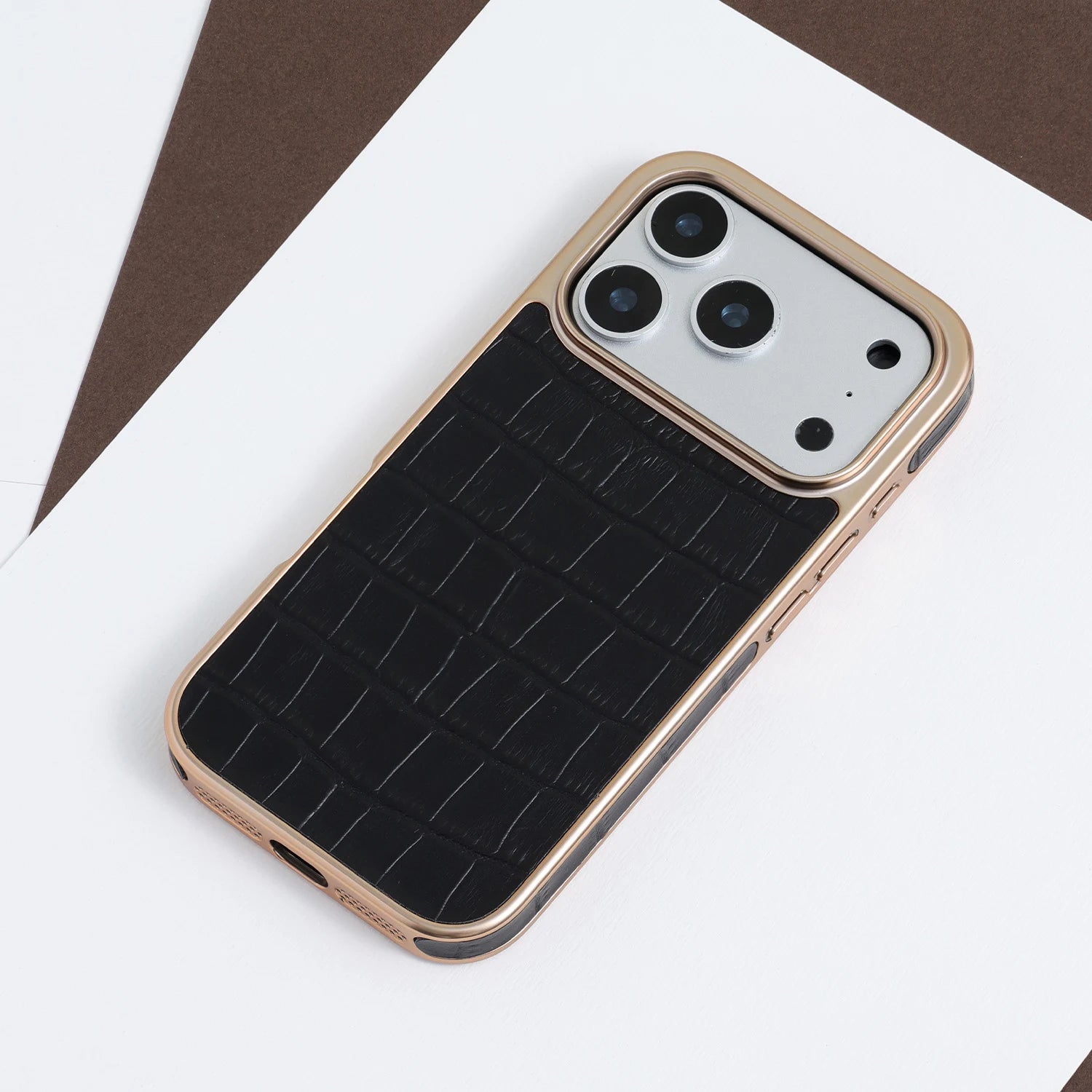 Black croc-embossed leather phone case with a champagne-gold border, styled on a white and brown geometric background.