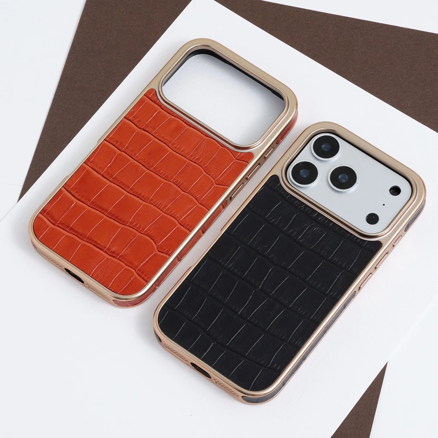 Amber-orange croc-embossed leather phone case with a champagne-gold border, styled on a white and brown geometric background.