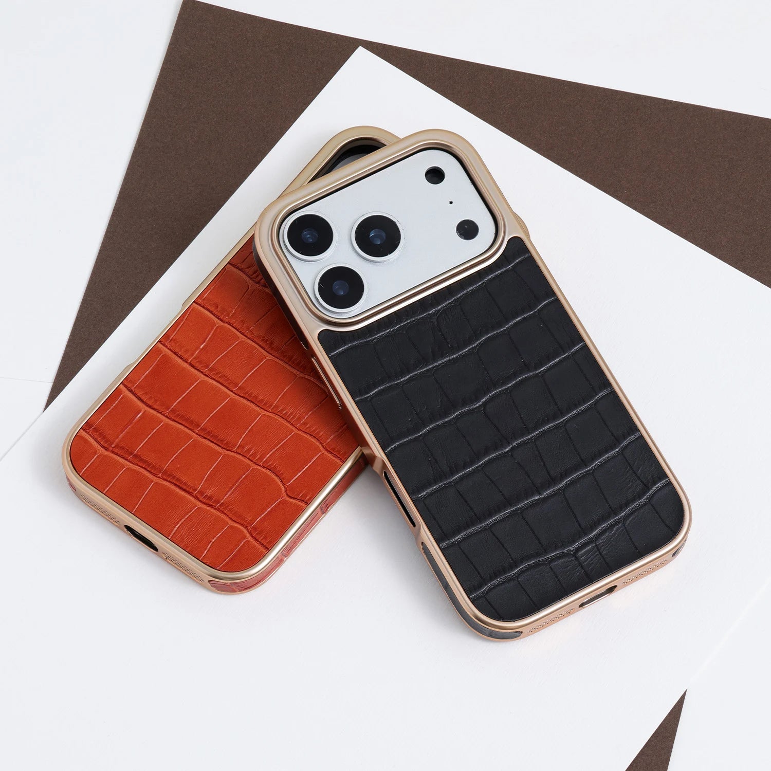 Two croc-embossed leather phone cases in black and amber with champagne-gold framed edges arranged side by side.