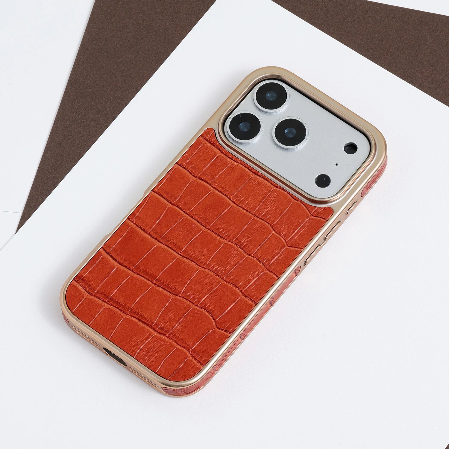 Croc-embossed leather phone case with a champagne-gold frame, shown in black and amber tones on a clean neutral background.