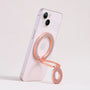 Rose gold MagSafe expandable metal ring stand attached to iPhone, sculptural circular design