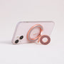 Rose gold MagSafe expandable metal ring stand attached to iPhone, sculptural circular design