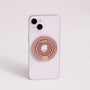 Rose gold MagSafe expandable metal ring stand attached to iPhone, sculptural circular design