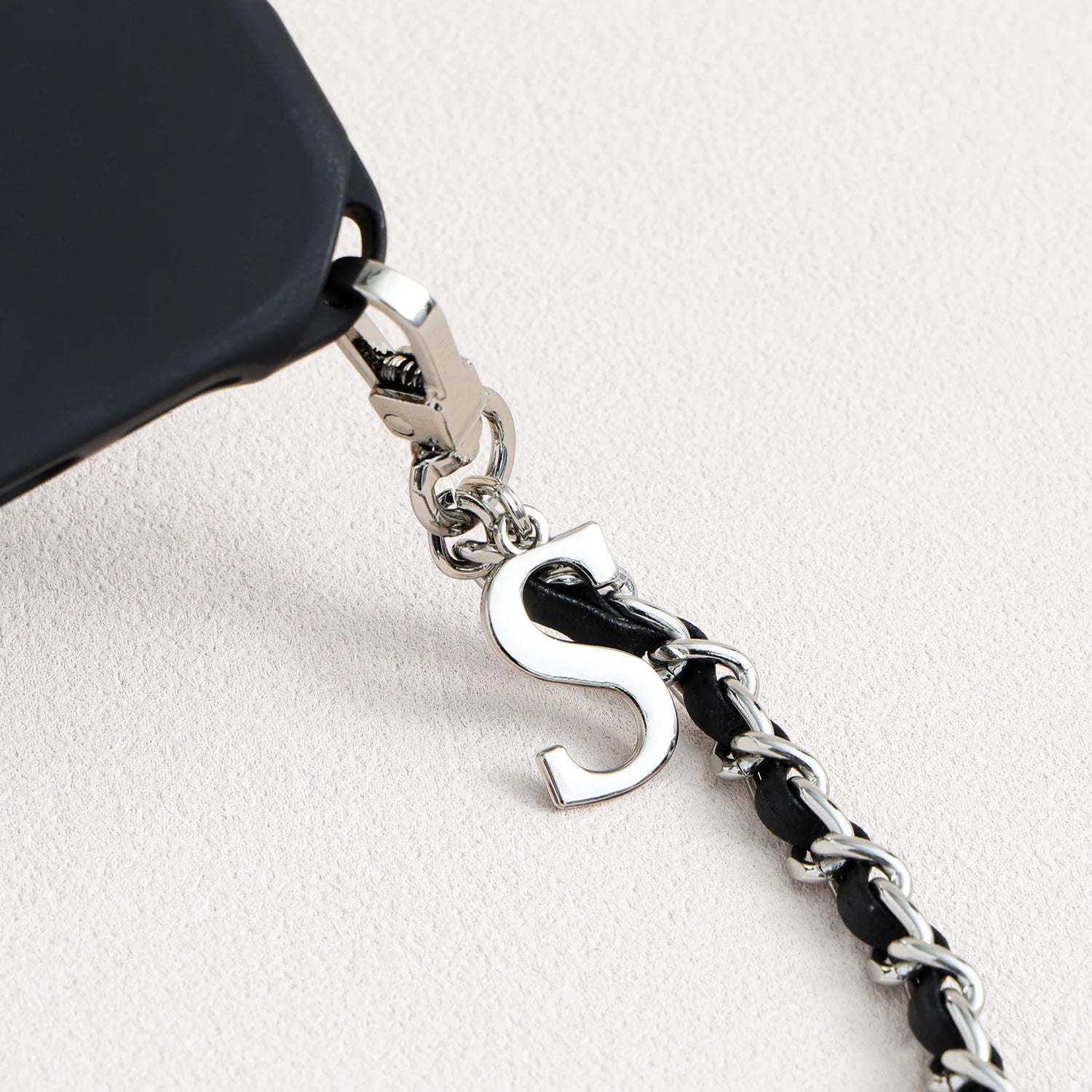 Close-up of polished letter charm on detachable leather-woven phone chain