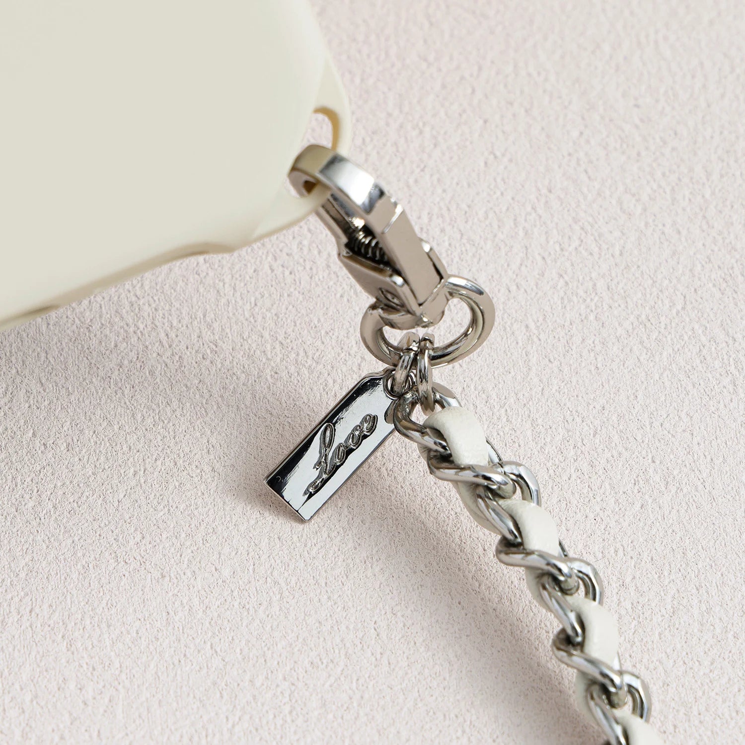 Detail of polished metal logo charm and leather-woven chain on phone case set