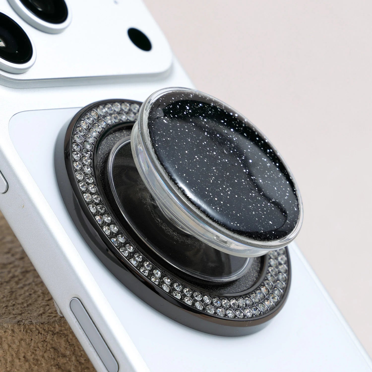 Close-up of the black phone grip stand featuring a glossy starry textured center and a ring of rhinestone embellishments.