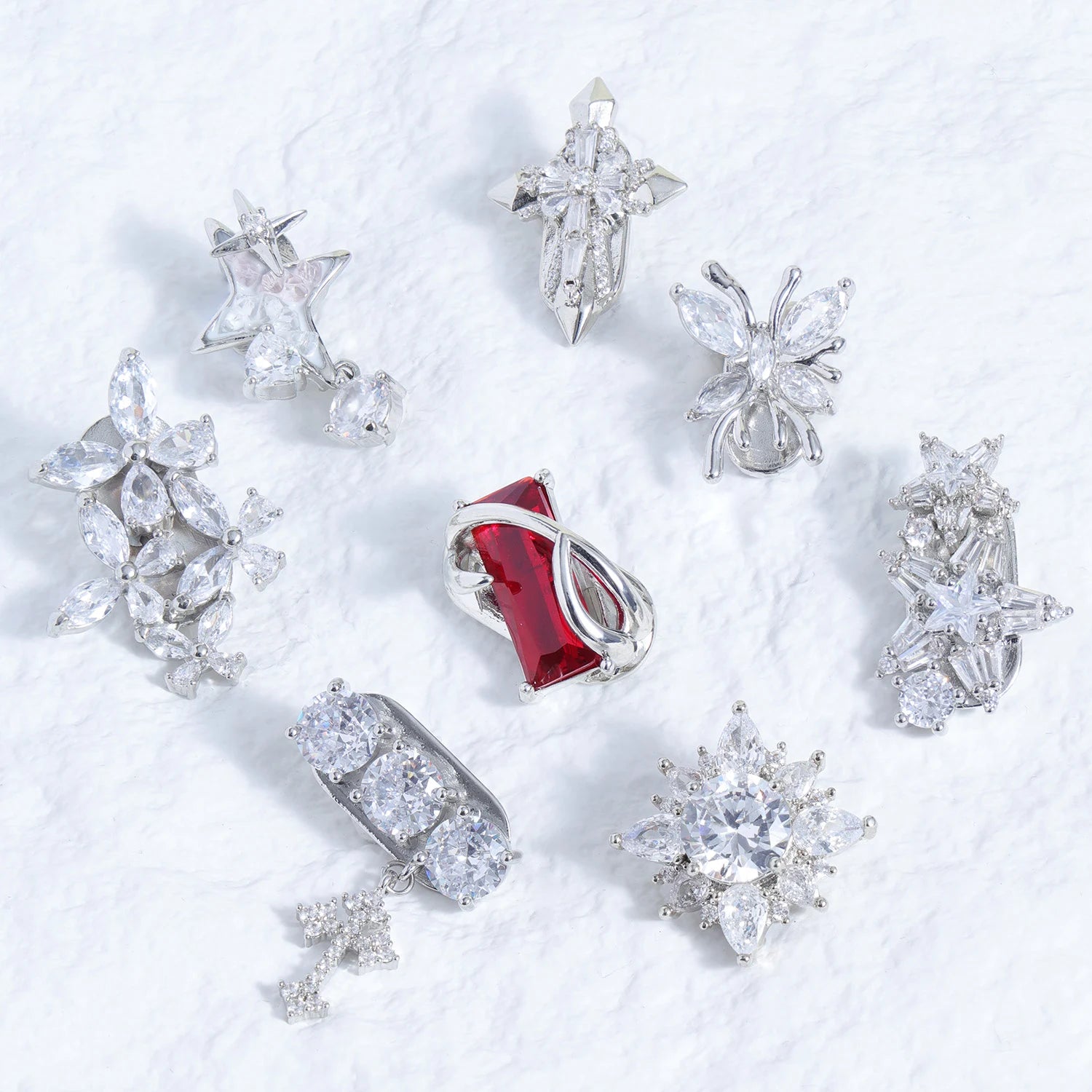 Assorted crystal magnetic ear charms including cross, floral, star, and red jewel designs on a white background