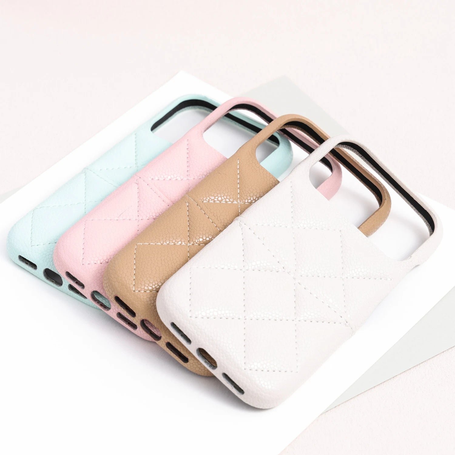 Four quilted leather phone cases in sky blue, powder pink, sand beige, and ivory arranged in a layered stack.