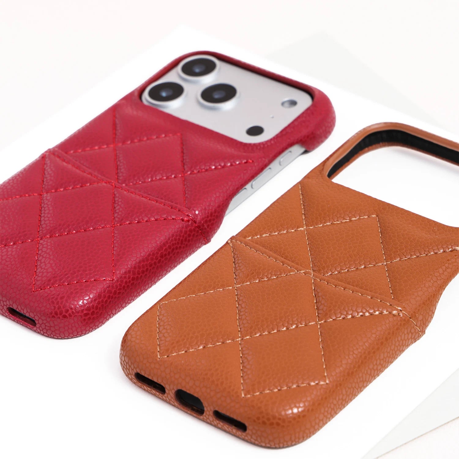 Close-up of a scarlet red phone case and caramel tan case highlighting the textured grain and stitched geometric pattern.