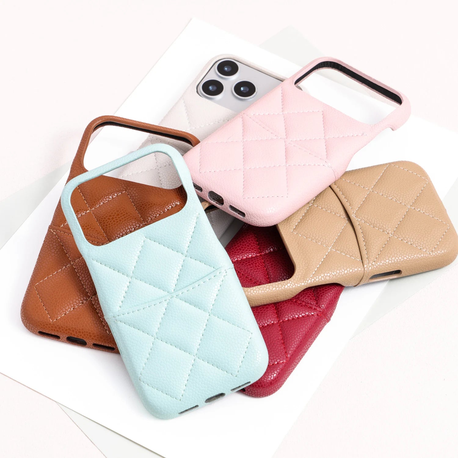Group display of multiple quilted leather phone cases in caramel, mint blue, ivory, pink, beige, and red.