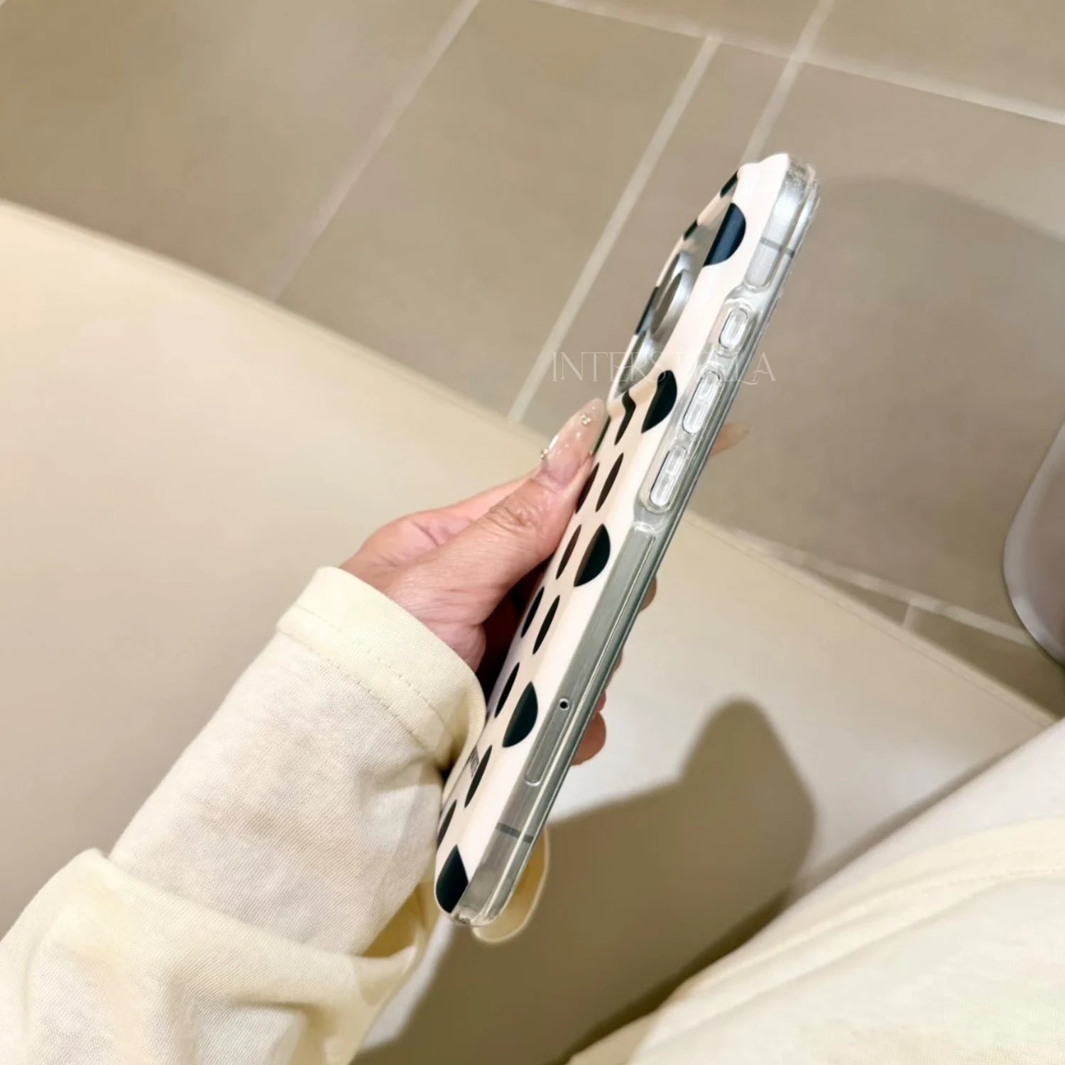 Angled side profile of an ivory phone case with bold black polka dots, highlighting the slim structure and clear edge.