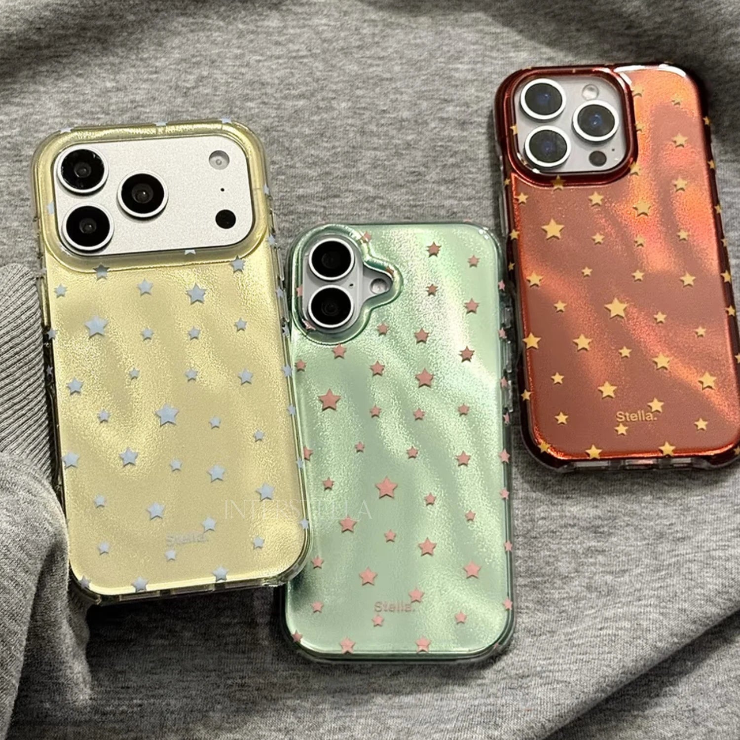 Three glossy star phone cases in gold, mint green, and deep red displayed on grey fabric