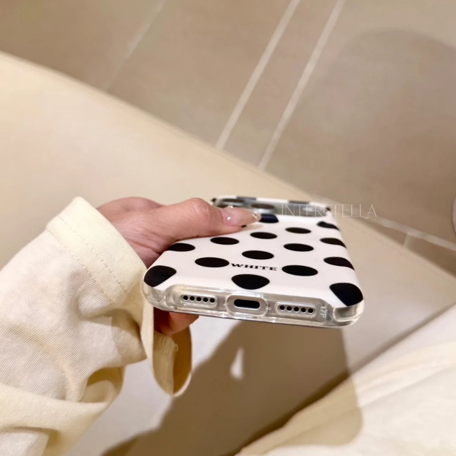 Bottom view of an ivory phone case with bold black polka dots, showing the charging port, speaker cutouts, and clear bumper.