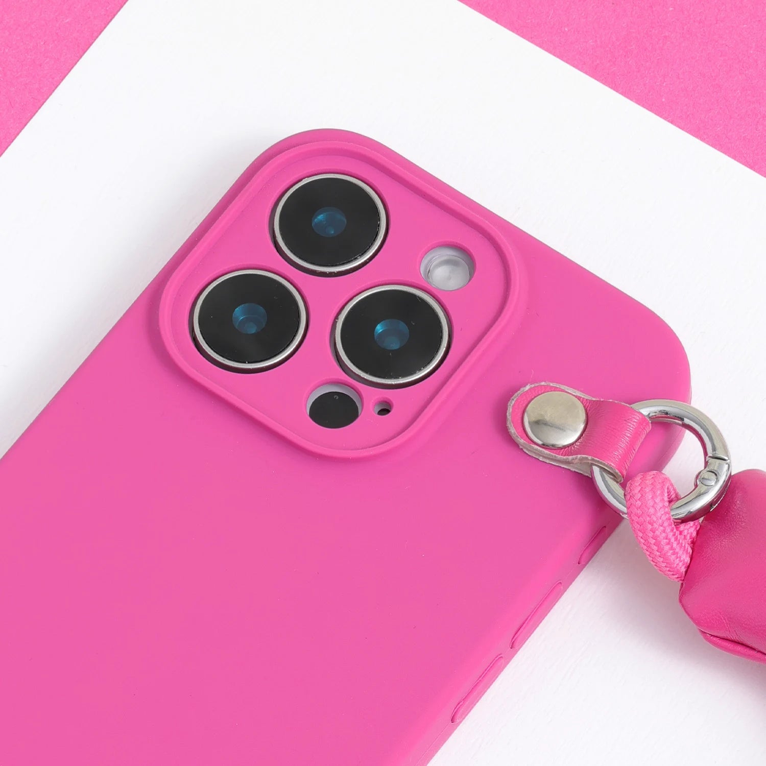Detail view of a vivid pink phone case showing the raised camera surround, smooth case body, and padded handle attachment.