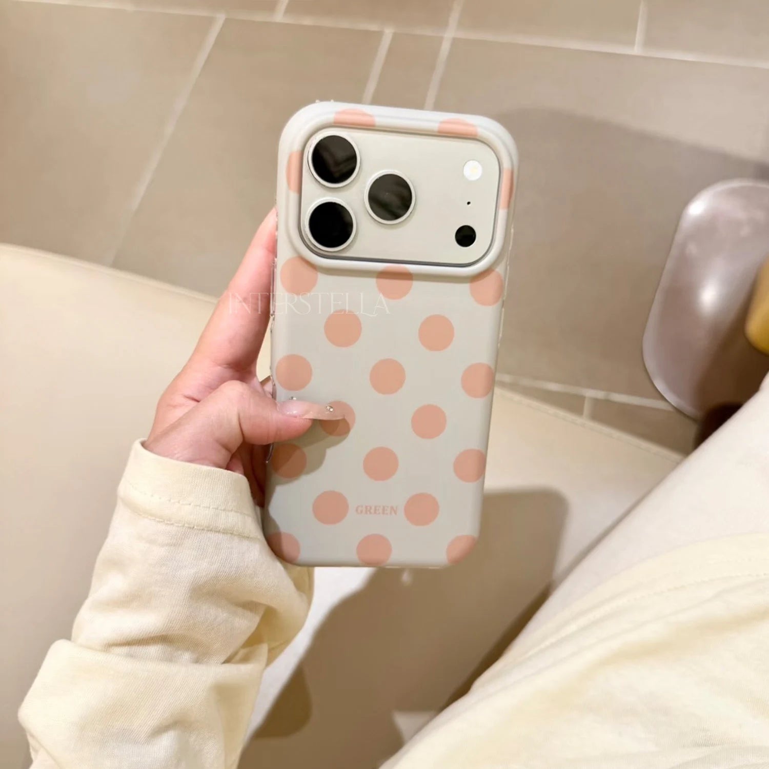 Hand holding a soft mint green phone case with warm beige polka dots and raised camera surround.
