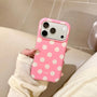 Hand holding a candy pink phone case with ivory polka dots and raised camera surround in a warm indoor setting.