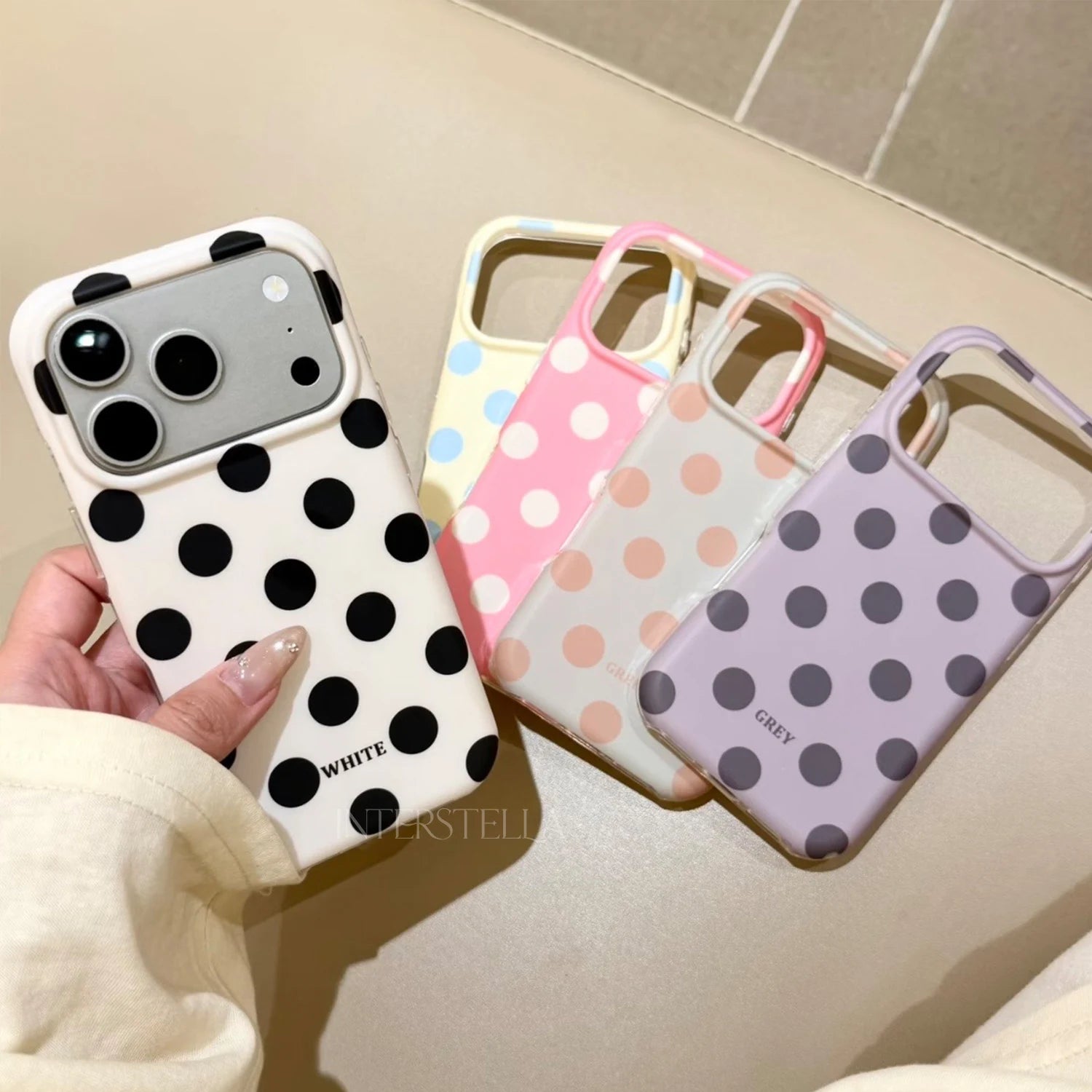 Hand holding the ivory black polka dot phone case with the yellow, pink, mint, and lilac colorways displayed beside it.