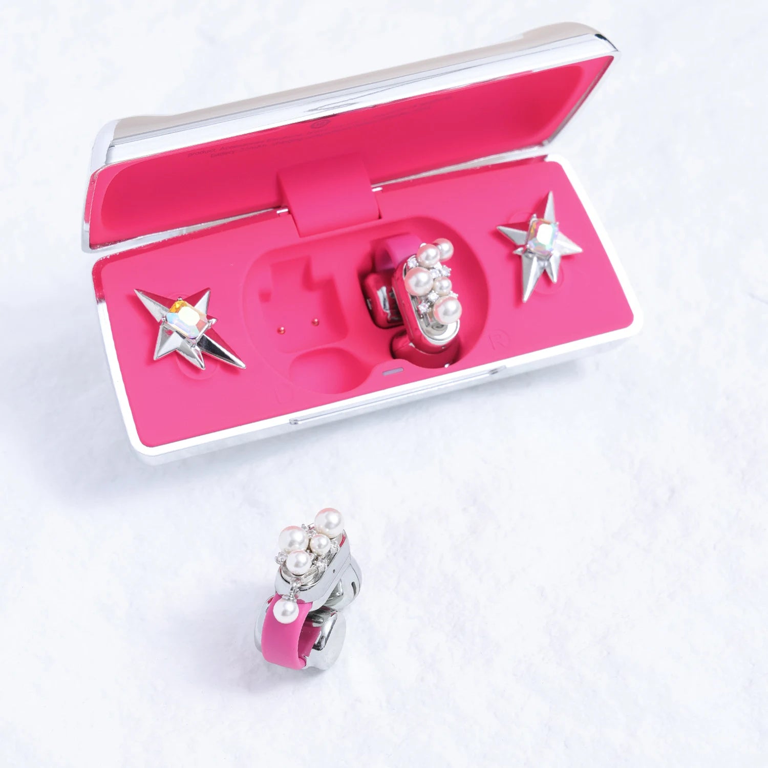 Open pink Interstella Aura charging case with pearl and Swarovski crystal ear charms, with one charm attached to a pink earbud outside the case.