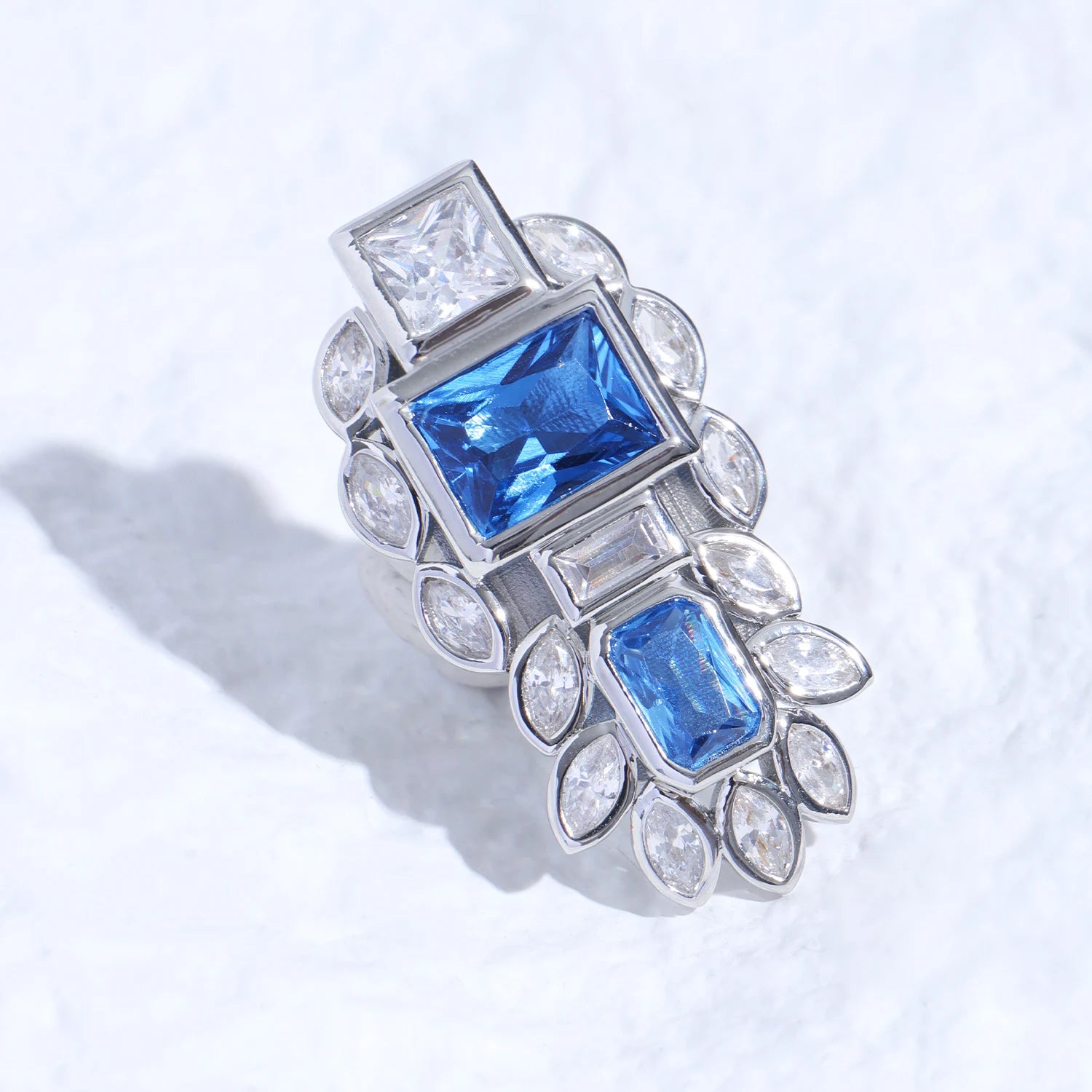 Blue gemstone ear charm with Swarovski crystal accents and silver-tone plated reliquary silhouette on a white textured surface