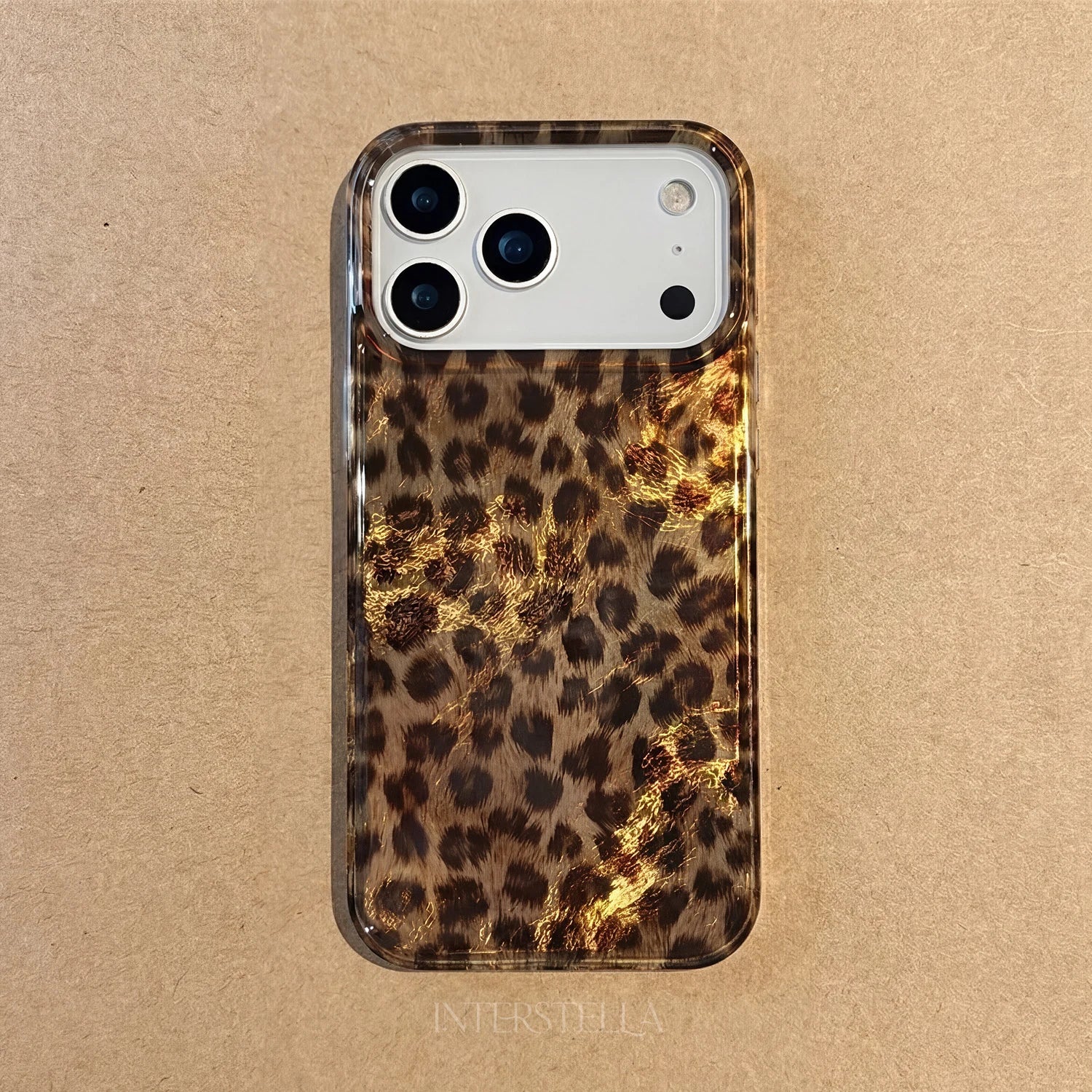 Hand holding a glossy petite leopard phone case in warm honey-brown tones with a refined small-scale animal pattern and raised camera surround.