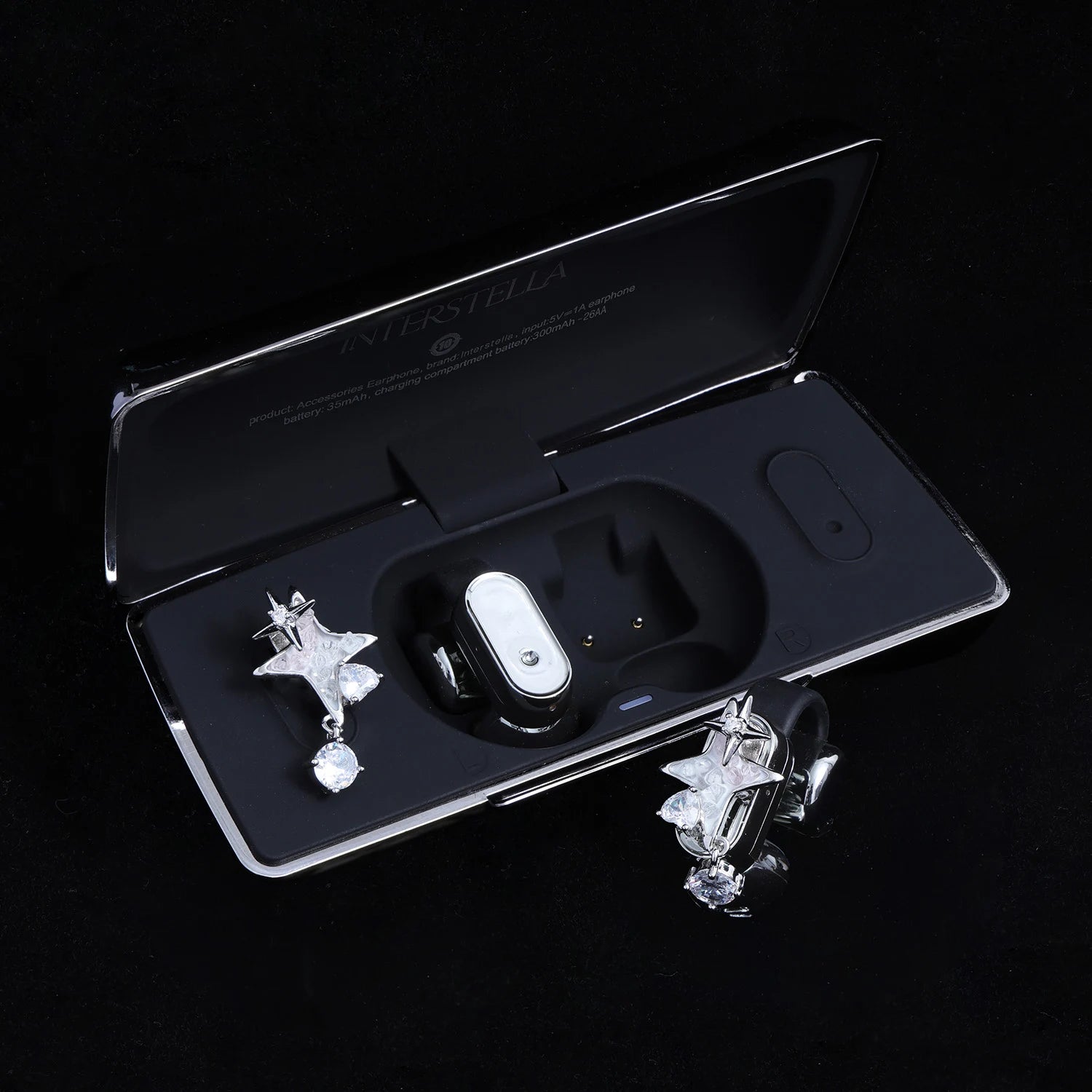 Silver-tone star ear charms with clear crystal drop displayed with black Interstella magnetic earphone charging case