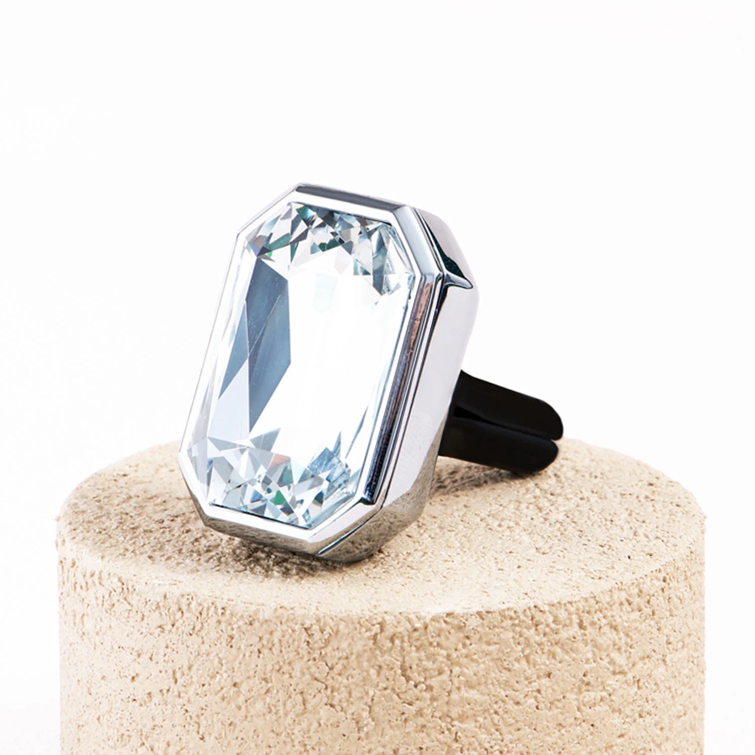 Palladio Prism crystal car diffuser displayed on a beige stone pedestal with a faceted rectangular crystal and polished silver frame