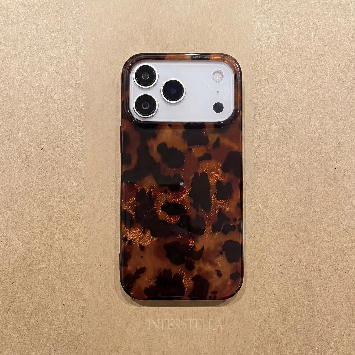 Tortoiseshell leopard phone case laid flat on a beige textured background