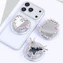 Three silver-tone mirror phone stands with pink crystal accents displayed together, featuring heart, cross-like, and ornamental frame silhouettes on circular bases.