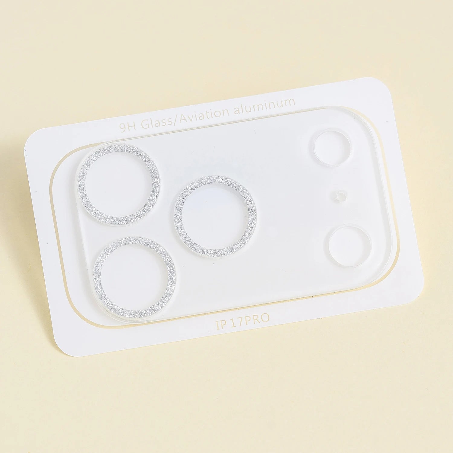 Clear acrylic camera lens protector with silver glitter rings around three camera lens openings, displayed on a pale background.