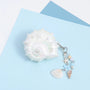 Closed iridescent conch-shaped AirPods case in opaline pearl white with embossed shell detailing and a dangling ocean charm chain with shells, beads, and starfish accents.