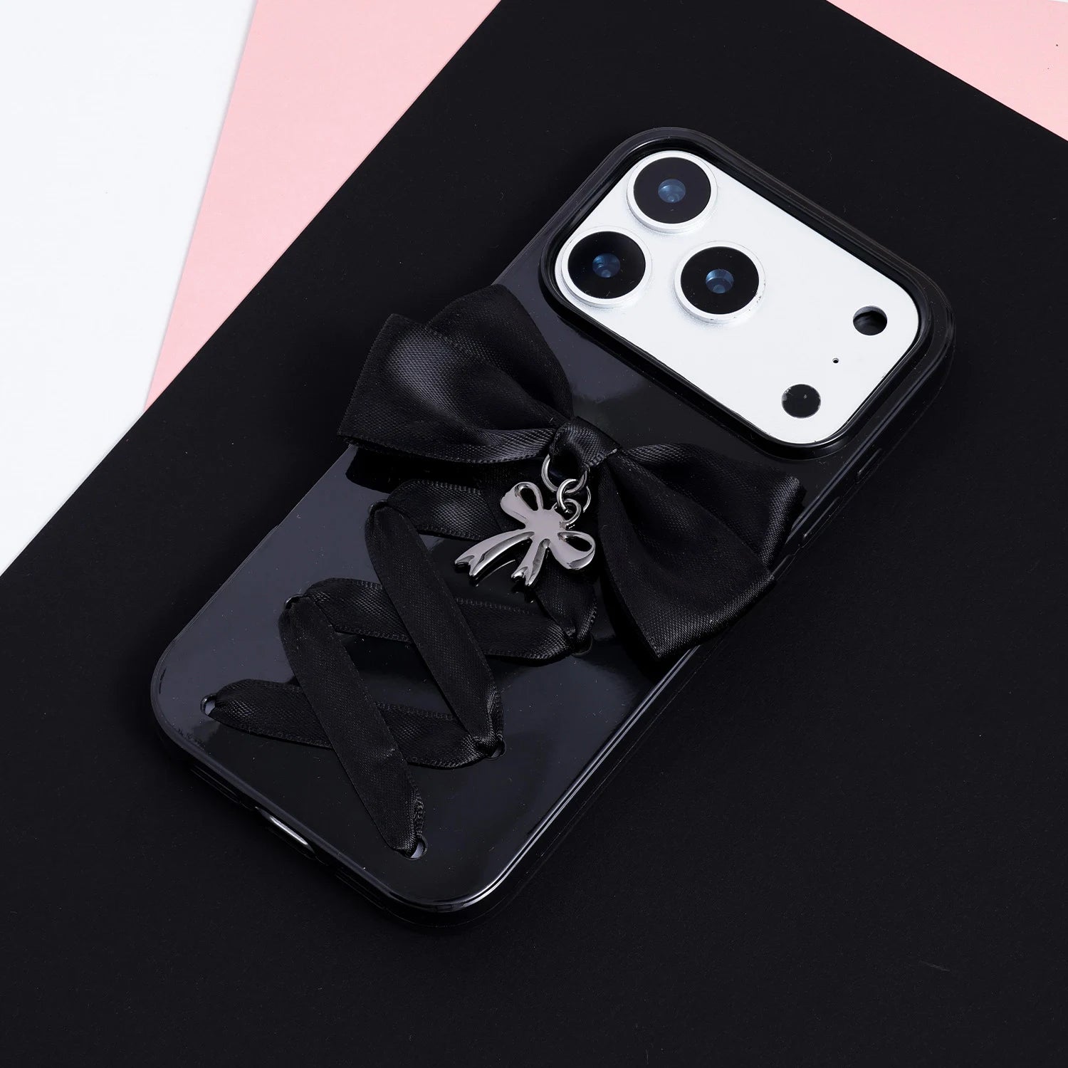 Full view of a black pendant ribbon phone case featuring a hand-finished bow, silver charm, and lace-up ribbon design against a dark background.