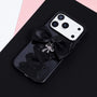 Full view of a black pendant ribbon phone case featuring a hand-finished bow, silver charm, and lace-up ribbon design against a dark background.