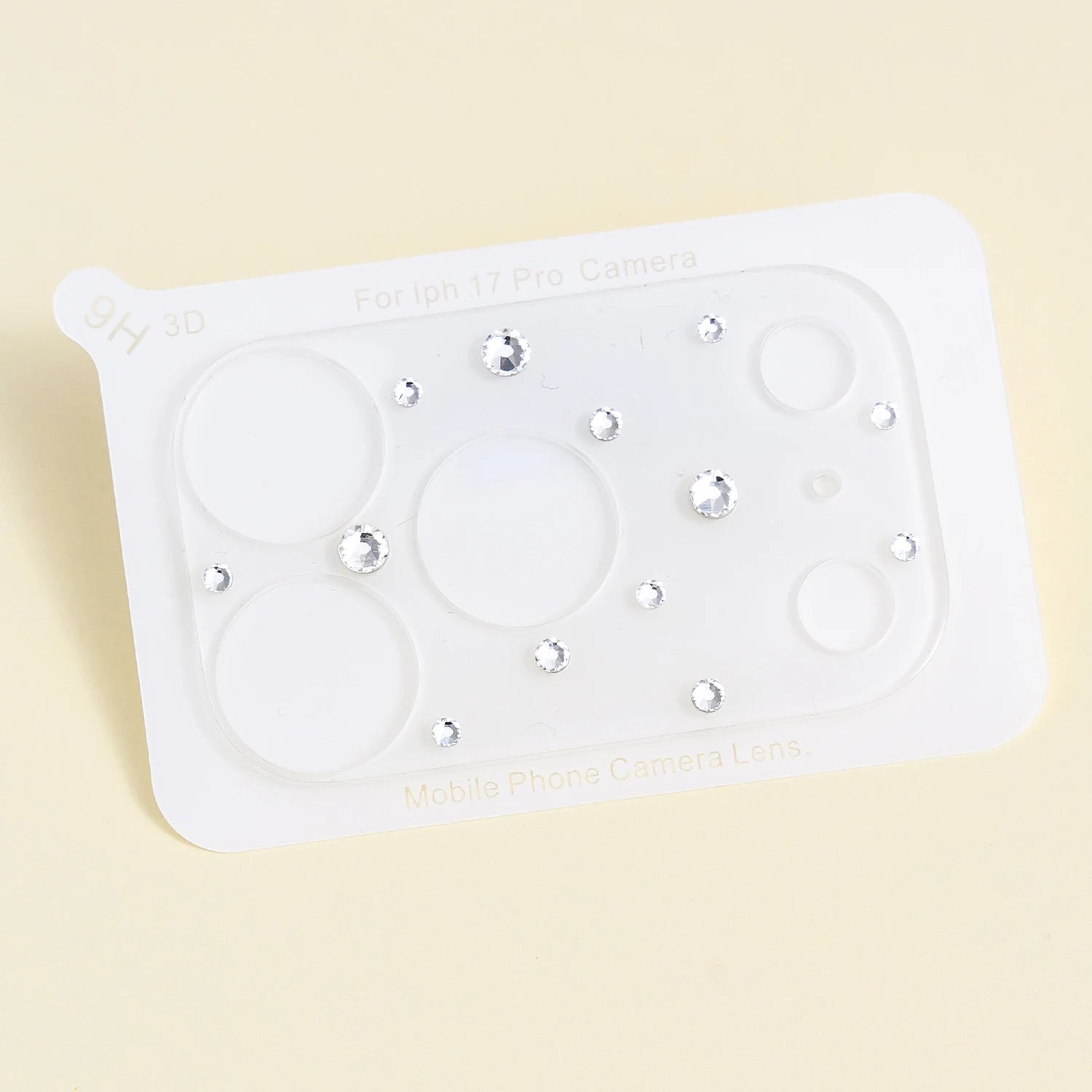 Clear acrylic camera lens protector sheet decorated with scattered silver crystals, displayed flat on a soft pale background.