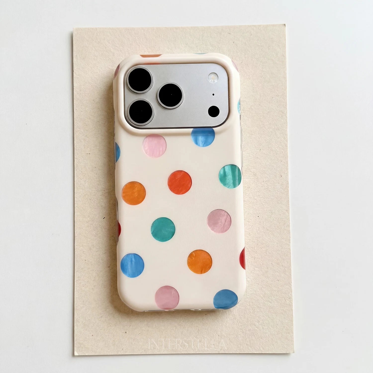 Ivory phone case with multicolor polka dots displayed on a textured cream paper background