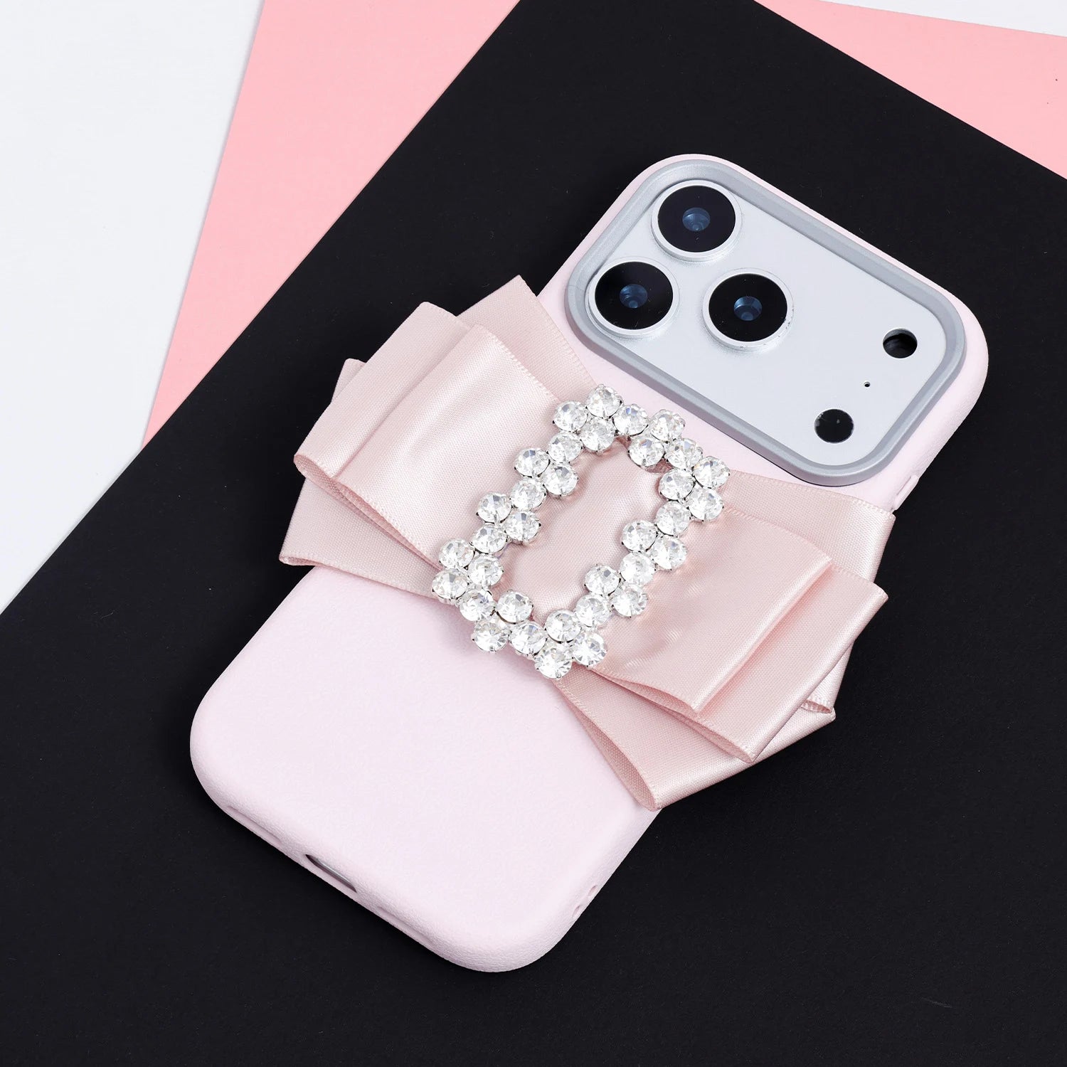Blush pink phone case featuring a handmade oversized satin bow with a crystal buckle centerpiece and raised camera surround.