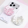 Ivory white and blush pink jewel bow phone grip stands displayed beside a pastel star-print phone case.