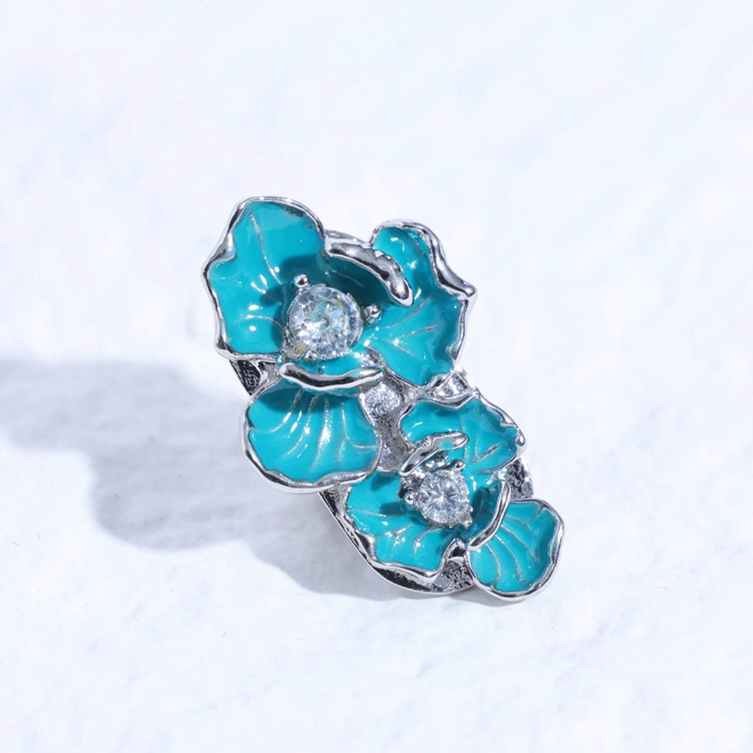 Single turquoise floral magnetic ear charm with silver-tone edges and crystal centers displayed against a soft white background.