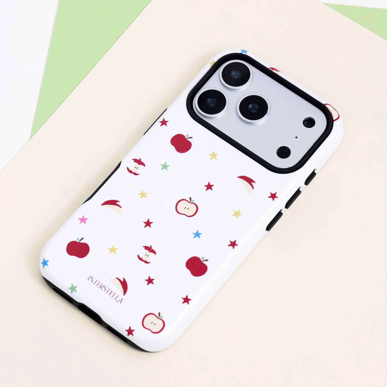 White dual-layer film-style phone case with red apple motifs, apple slices, and multicolored stars, finished with a contrasting black camera surround.