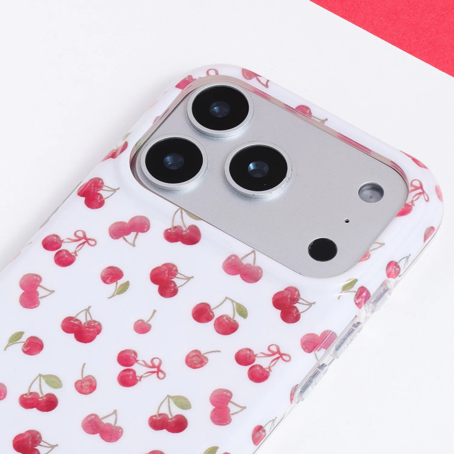 Close-up of a white cherry phone case showing tiny red cherries, soft green leaves, and a neat polished printed finish.