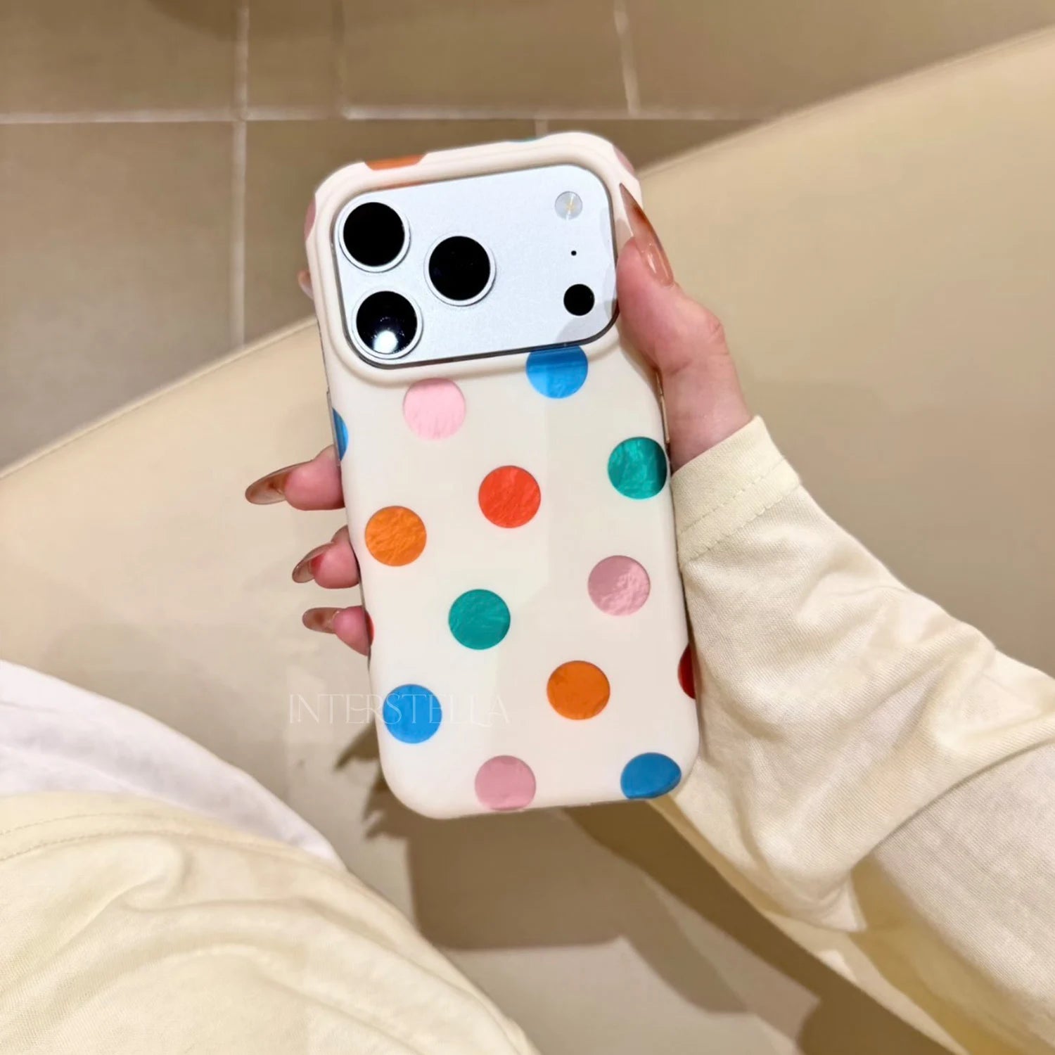 Hand holding an ivory phone case with painterly multicolor dot pattern