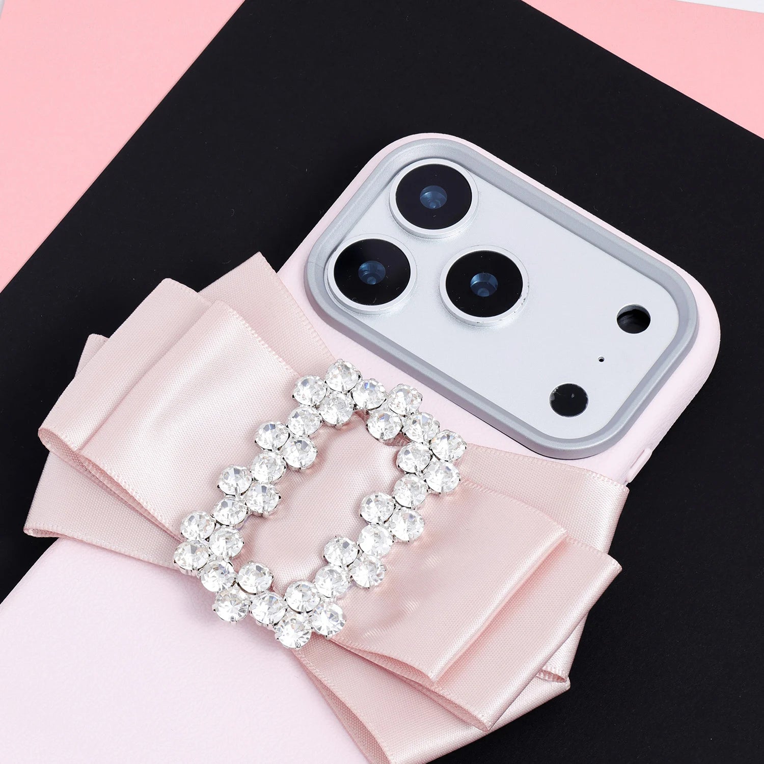 Close-up of a blush pink handmade ribbon phone case showing the satin bow folds, sparkling crystal buckle, and soft pink case body.