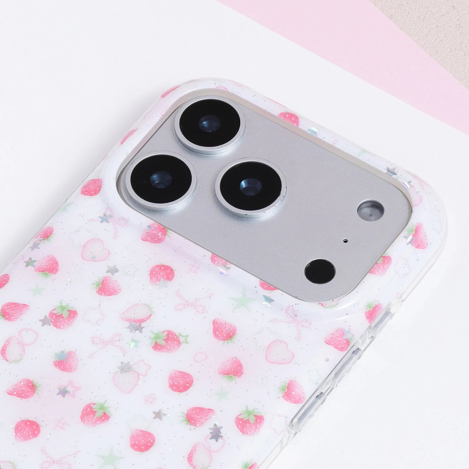 Close-up of a white strawberry phone case showing pastel fruit motifs, silver-toned star accents, and delicate decorative print details.