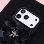 Close-up of a black handmade ribbon phone case showing the satin bow, silver pendant charm, glossy dark surface, and raised camera surround.