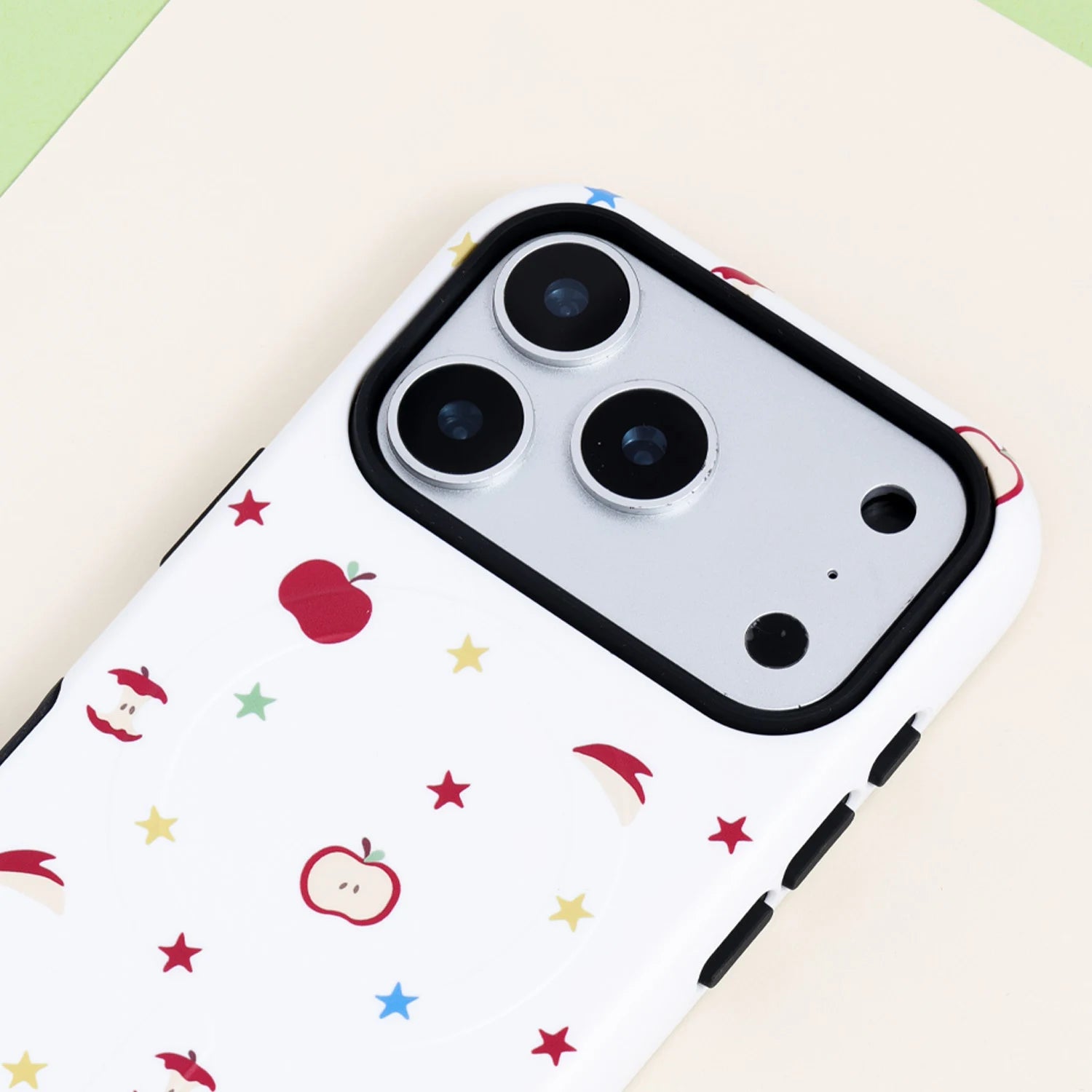 Close-up of an orchard-inspired apple print phone case showing the white background, red fruit motifs, colorful stars, and black raised camera frame.