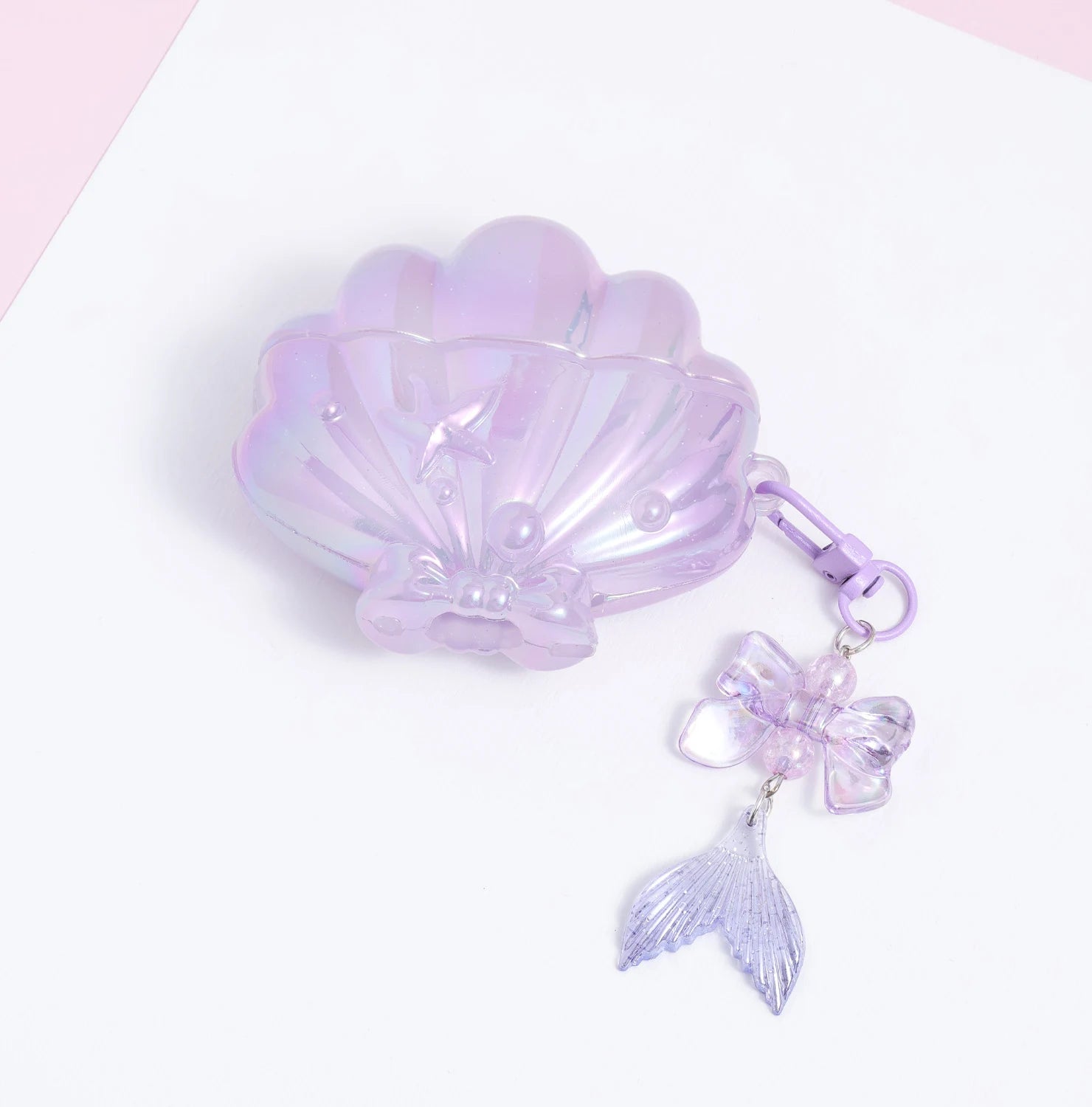 Closed lilac shell AirPods case with a glossy translucent finish, pearl and starfish detailing, and a dangling bow-and-mermaid-tail charm.