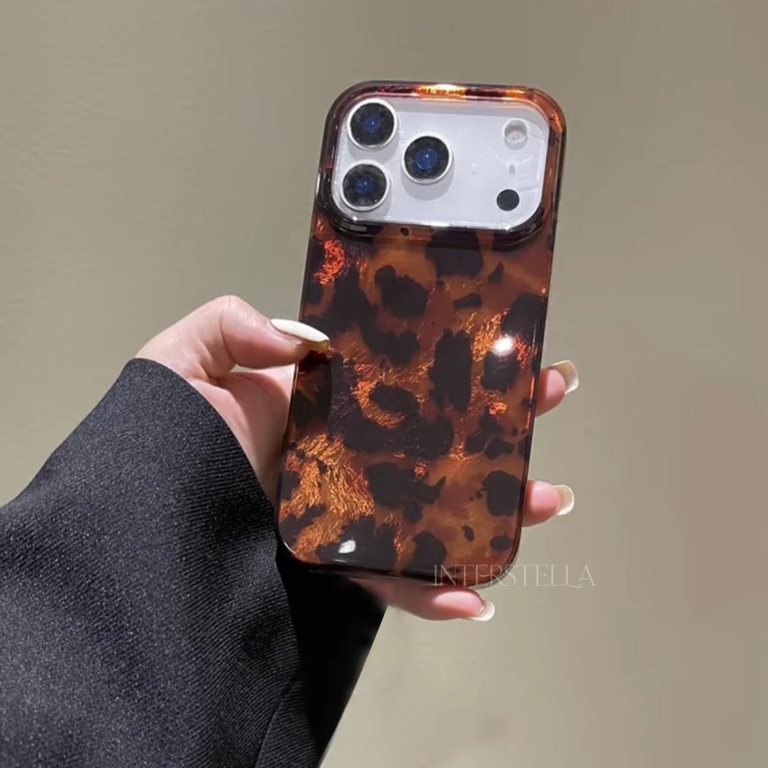 Hand-held view of a glossy amber brown leopard print phone case with bold black pattern