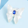 Front view of a white 3D-printed bow phone stand with smooth sculptural folds and a faceted blue jewel centerpiece on a pale blue background.