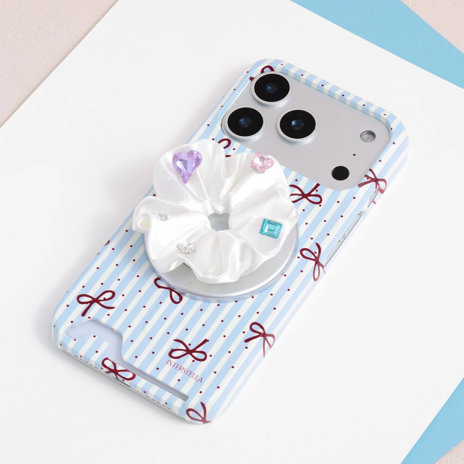 White jewel rosette phone grip stand mounted on a blue-and-white striped bow card-slot phone case.